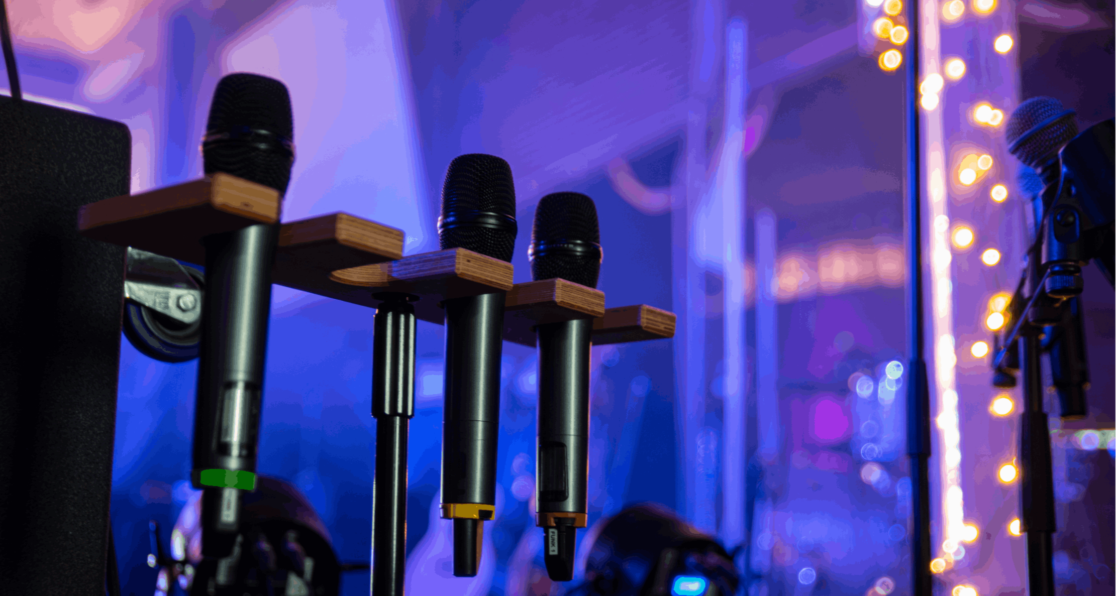 Wireless microphones racked backstage with stage lighting behind — professional audio and live event production management